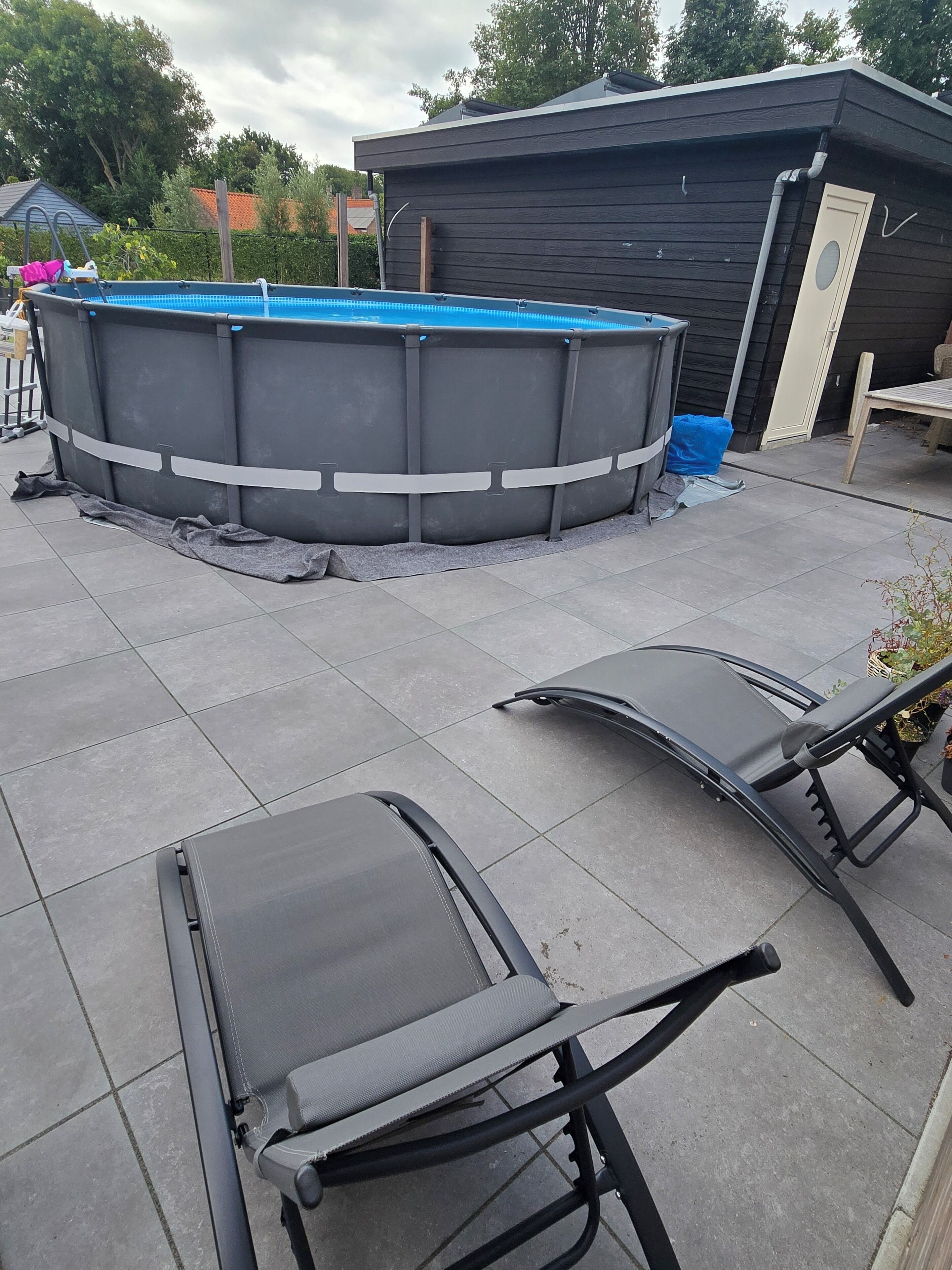 An outdoor swimming pool area with a covered hot tub, a lounge chair, and a small building.