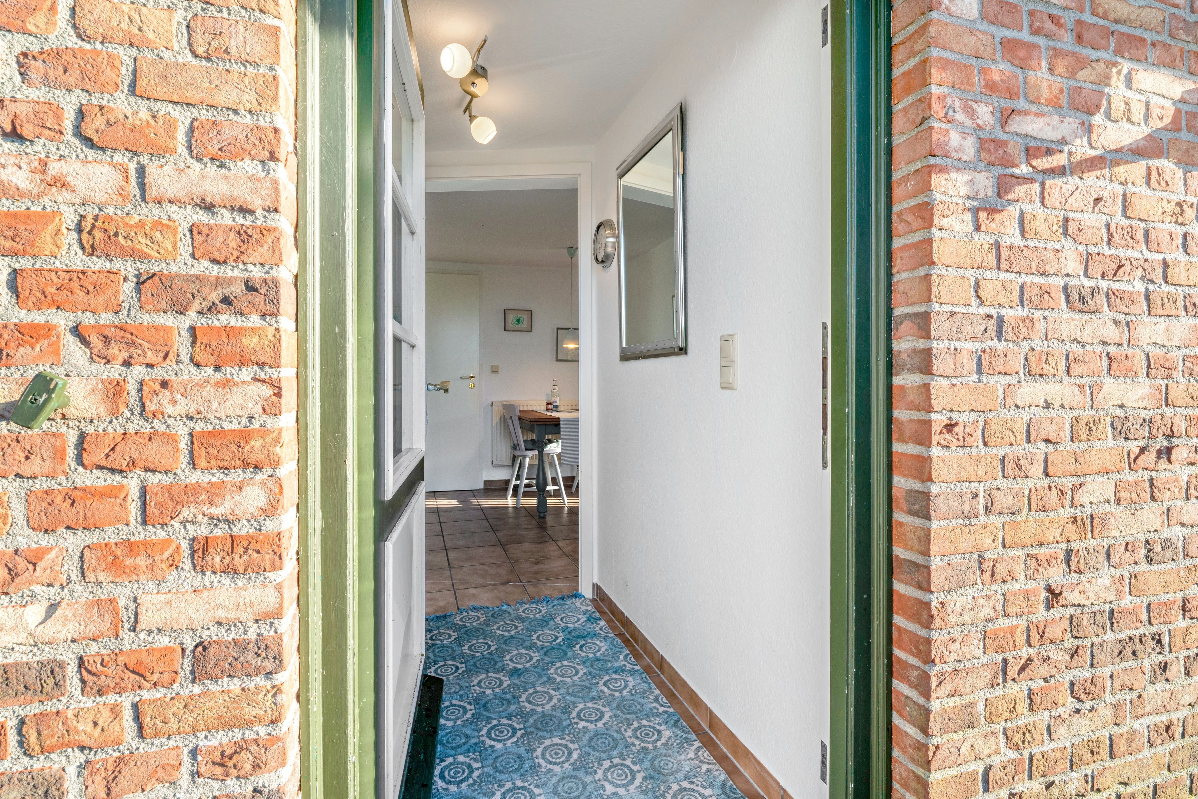 Un couloir avec un tapis à motifs, une porte donnant sur une pièce et un mur en briques.