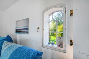 A room with a bed, a window with a view of greenery, and a painting on the wall. - Nordermühle Apartment with Shared Garden, Terrace and Wi-Fi (Pellworm)