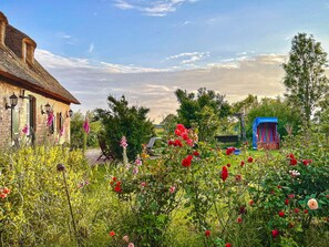 A brick building with a thatched roof, a garden with various flowers, and a blue play structure. - Nordermühle Apartment with Shared Garden, Terrace and Wi-Fi (Pellworm)