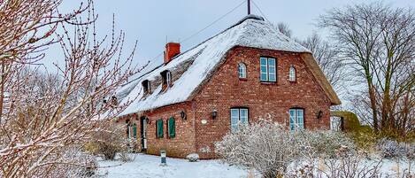 A brick house with a steeply pitched roof, multiple windows, and a chimney.
