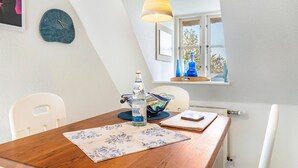 Un coin repas avec une table en bois, une bouteille d’eau, un bol et une fenêtre donnant sur des arbres.