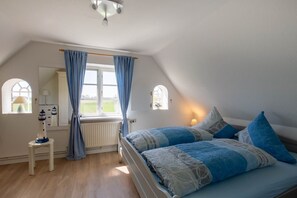 Een slaapkamer met een bed, een raam met gordijnen, een lamp en een kleine tafel.
