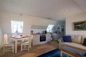 Een ruimtelijk ingerichte leefruimte met een eethoek, kitchenette en een bank.