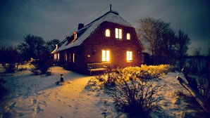 Une maison recouverte de neige, avec un banc à l’extérieur, un toit enneigé et un ciel dégagé.