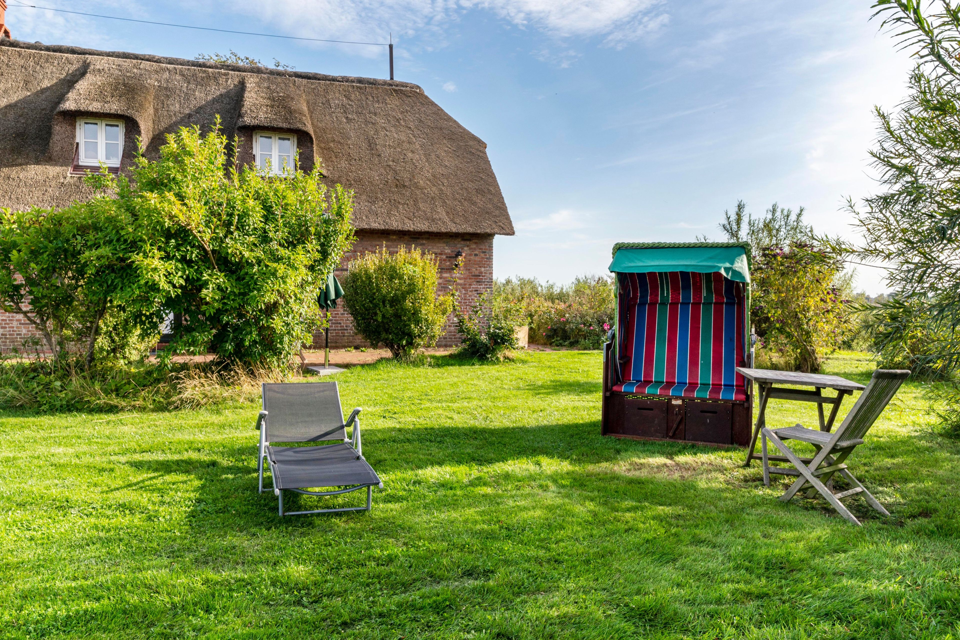 Ein Rasen mit einem Haus mit Strohdach, einer kleinen Gartenhütte und zwei Stühlen.