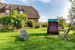 Een gazon met een rieten huis, een kleine schuur en twee stoelen.