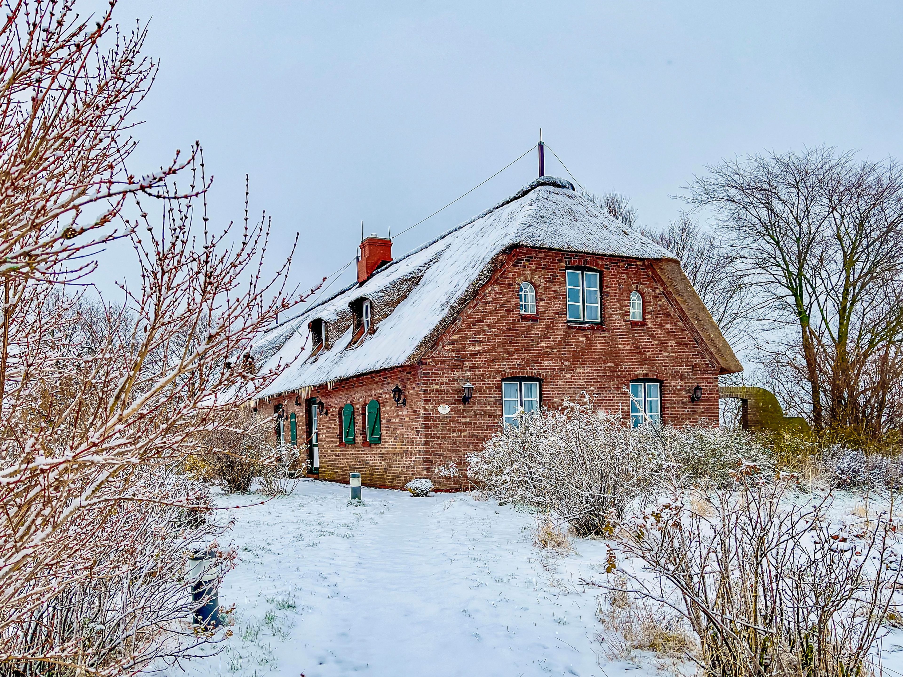 Ein Haus aus Backsteinen mit einem steilen Satteldach, zahlreichen Fenstern und einem Schornstein.