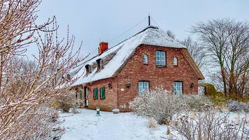 Ein Haus aus Backsteinen mit einem steilen Satteldach, zahlreichen Fenstern und einem Schornstein.