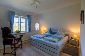 Un dormitorio con cama, una silla, una ventana, una lámpara y un estante en la pared.
