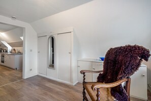 Une pièce avec une chaise en bois, une armoire blanche et un coin cuisine à l’arrière-plan.
