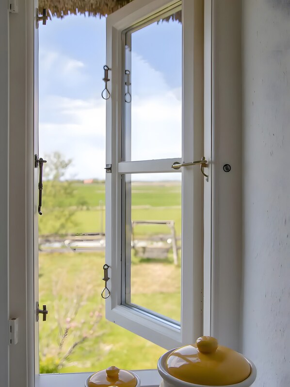 Een open raam met uitzicht op een grasveld en een houten gebouw.