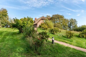 Une maison traditionnelle à toiture de chaume, entourée d’une végétation luxuriante et sous un ciel dégagé.