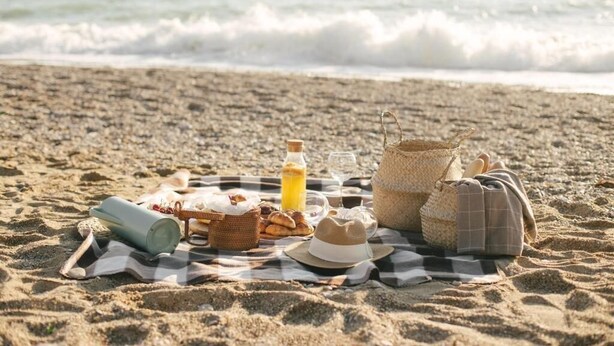 Ein Strandpicknick mit Decke, Speisen, Getränken und einem Hut.