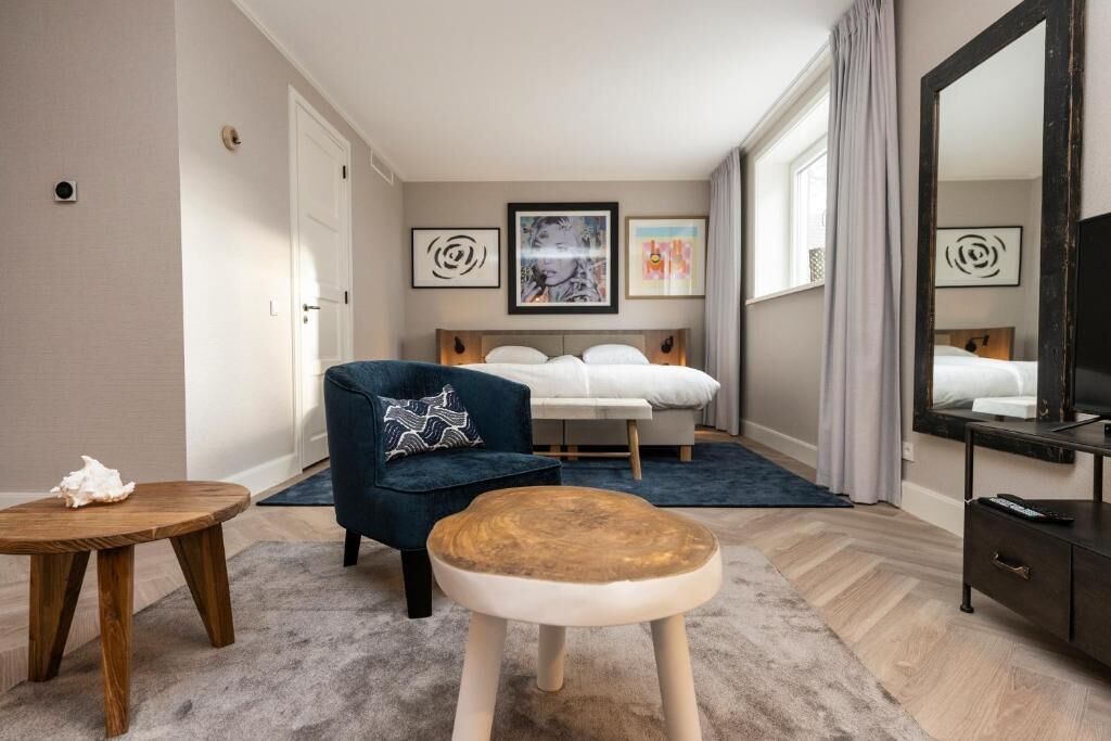 Une chambre d’hôtel avec un lit, une chaise, une petite table et des œuvres d’art accrochées aux murs.