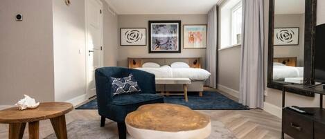 Une chambre d’hôtel avec un lit, une chaise, une petite table et des œuvres d’art accrochées aux murs.