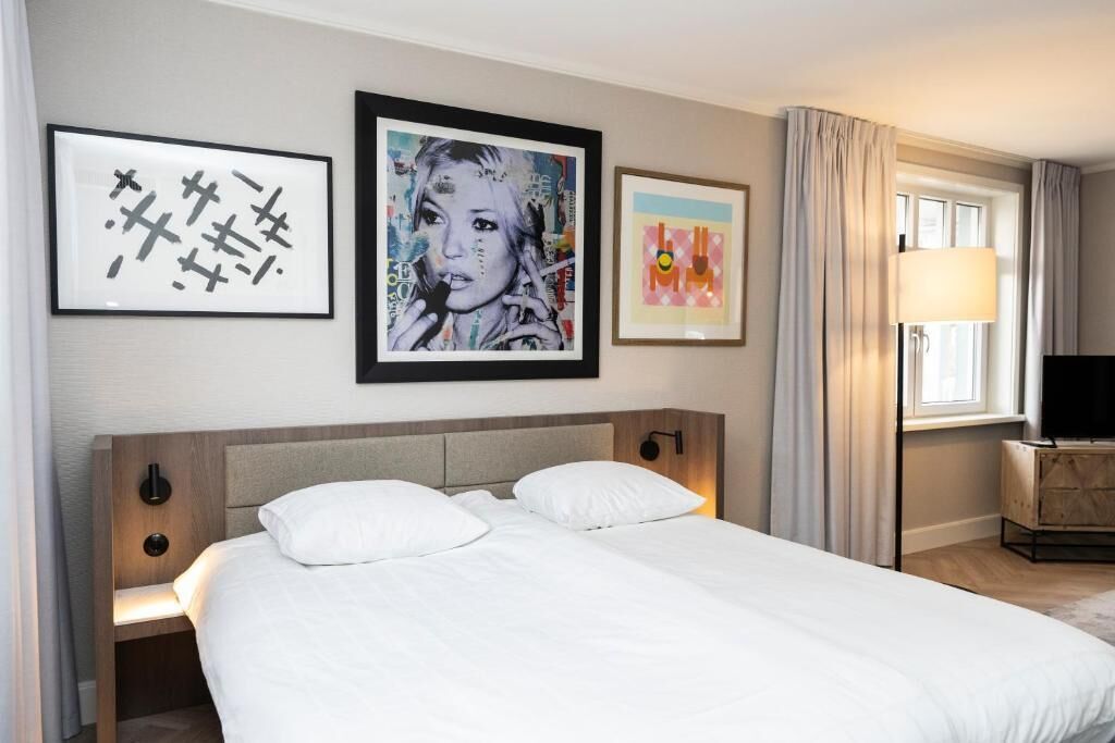 Habitación de hotel con cama, mesita de noche, lámpara y tres cuadros en la pared.