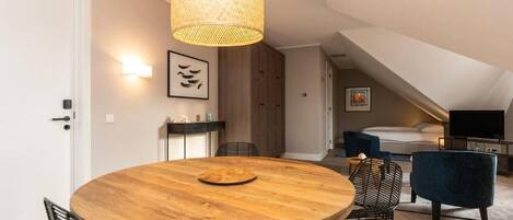 Un dormitorio tipo loft moderno con una cama grande, un televisor y un comedor con una mesa redonda de madera y sillas.