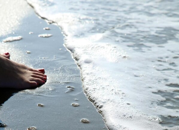 A close-up of a beach with a person's foot on the wet sand near the water's edge.