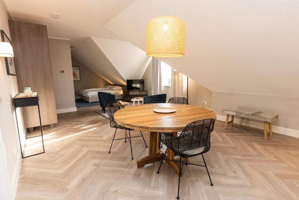 A modern dining area with a round wooden table, black wire chairs, and a woven pendant light.