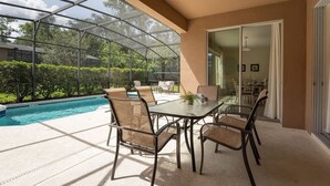 Un patio couvert avec une structure en verre, une piscine et du mobilier d’extérieur.
