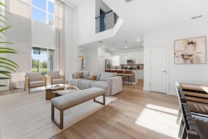 A spacious living room with a high ceiling, a built-in kitchen, and a dining area. - Reunion 5BR Home w/ Pool – 15min to Disney (Kissimmee)