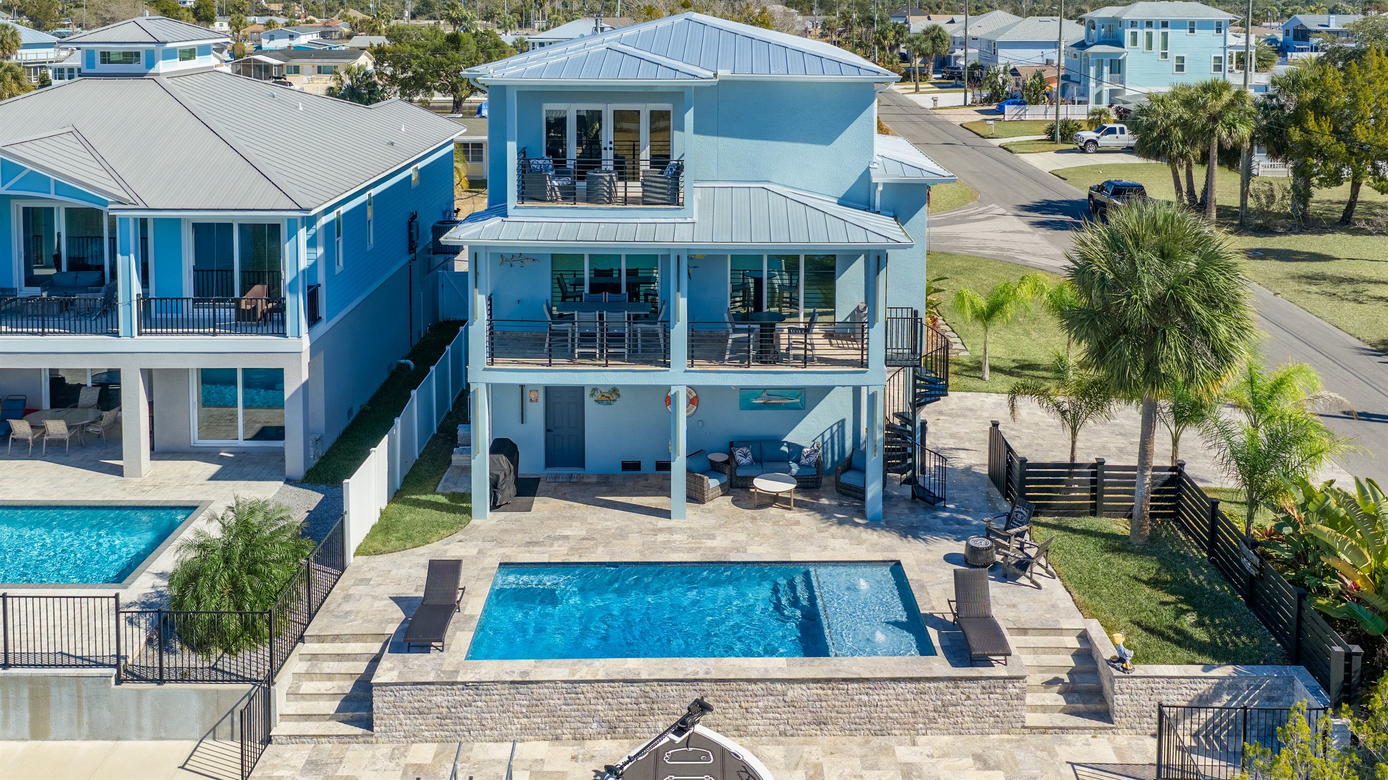 A multi-story beachfront property with a swimming pool, outdoor seating, and a view of the ocean.