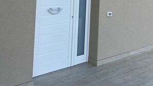 A white door with a handle and a frosted glass panel, a small wall-mounted light fixture above it, and a textured beige wall. - Villa Vittoria, brand new with pool and garden, near the sea, in Cinisi (Palermo)