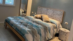 A bedroom with a bed, a bedside lamp, a mirror, and a window with blinds. - Villa Vittoria, brand new with pool and garden, near the sea, in Cinisi (Palermo)