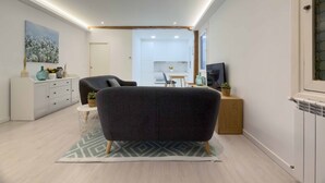 A modern living room with a dark armchair, a white cabinet, a dining area, and a kitchen in the background. - Usandizaga | The Rentals Collection (San Sebastián/Donostia)