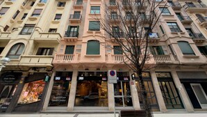 A multi-story building with a row of shops on the ground floor, including a visible storefront with signage. - Usandizaga | The Rentals Collection (San Sebastián/Donostia)