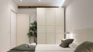 A hotel room with two beds, a small bedside table with a lamp, a plant, and a wardrobe. - Usandizaga | The Rentals Collection (San Sebastián/Donostia)