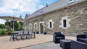 Un edificio de piedra con un patio de grava, mobiliario exterior y una zona cubierta con una sombrilla.