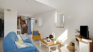 Una sala de estar con sofá, mesa de centro, televisor, escalera y puerta que da a otra habitación.