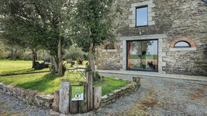 A stone building with a glass door, a wooden sign, and a grassy area with trees. - Gîte - Le Buis de Bréhaut: terrace, garden, and Wi-Fi (Taupont)