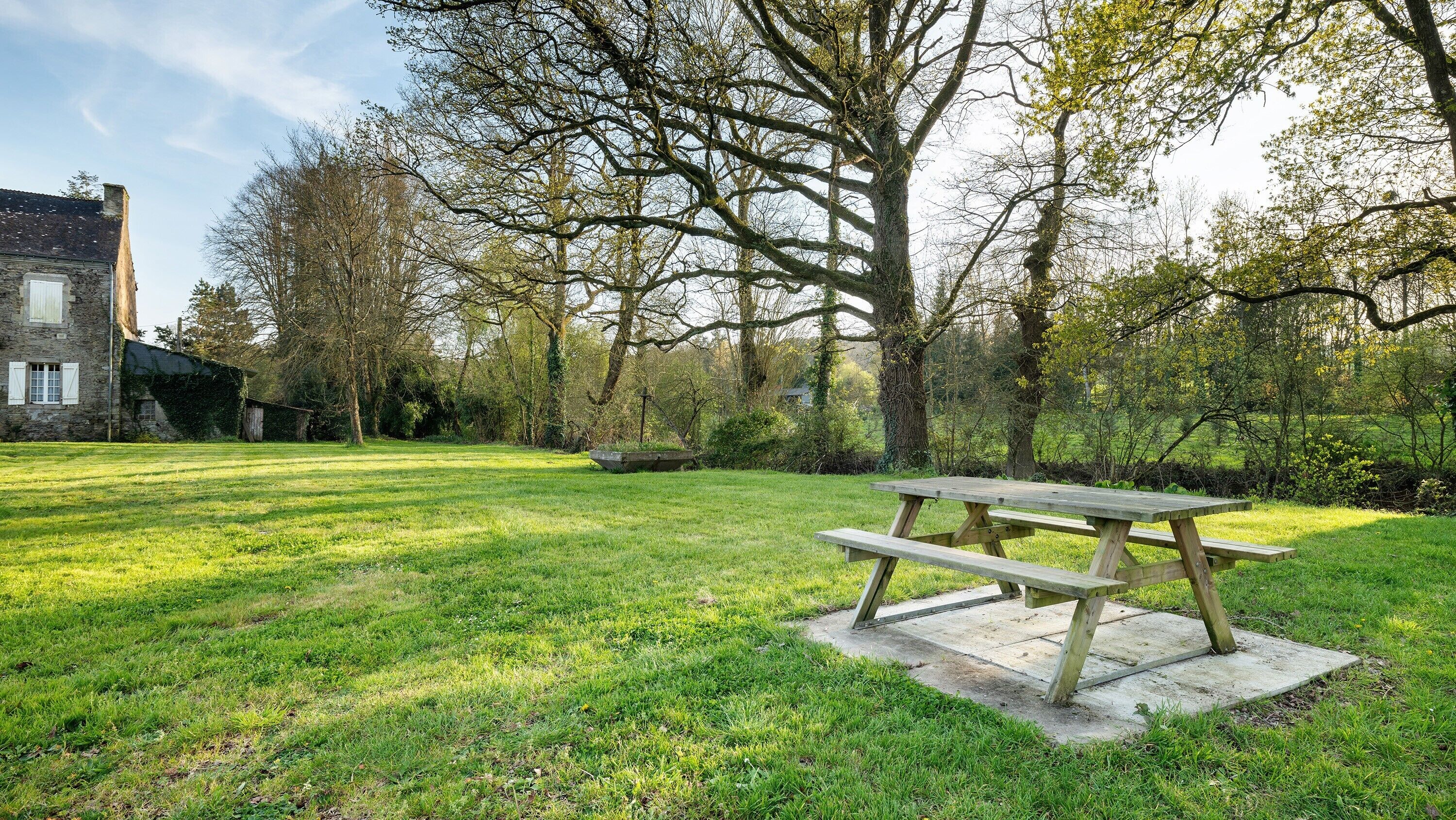 Een picknicktafel in een gazon met bomen en een stenen gebouw op de achtergrond.