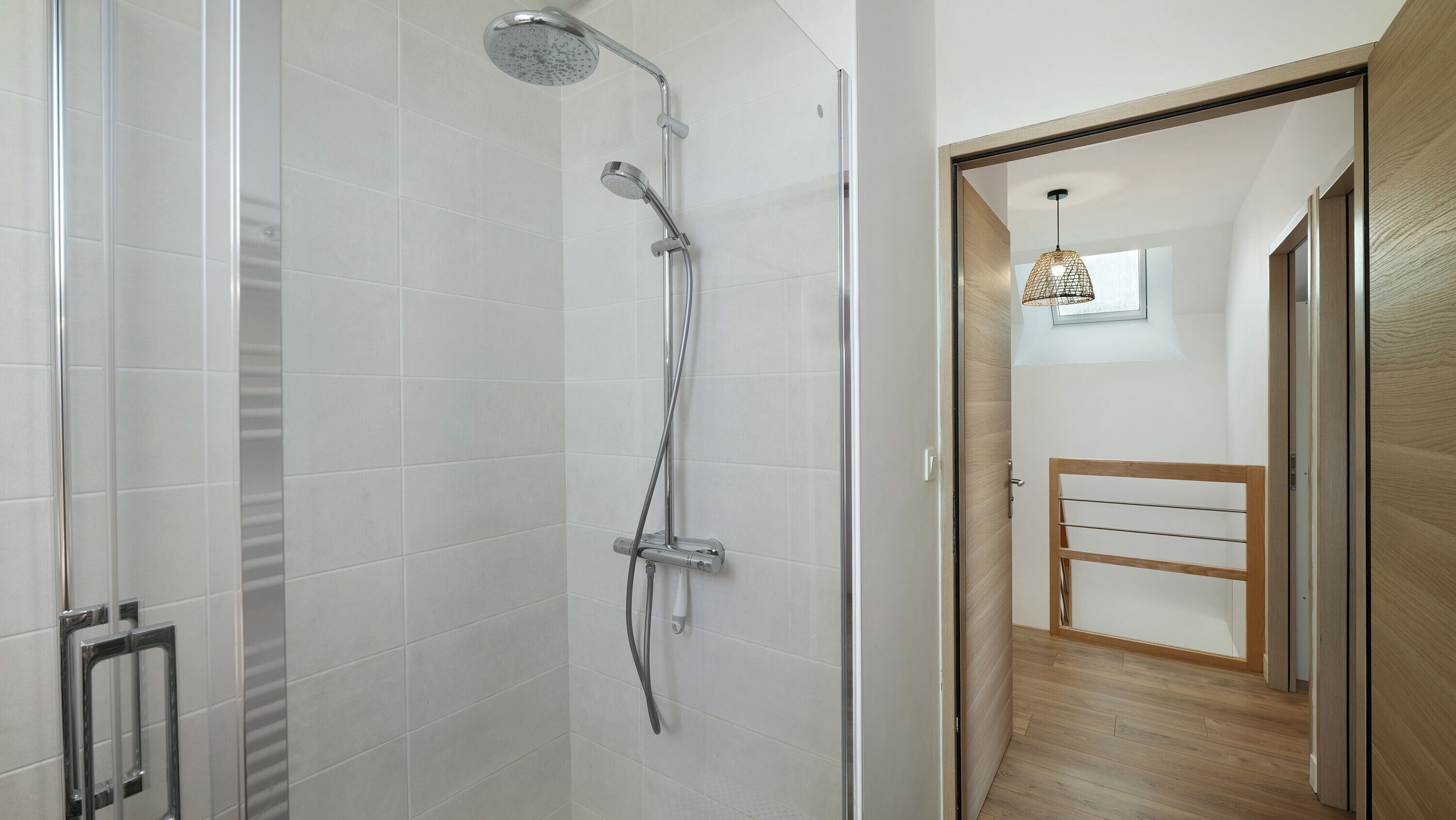 Una ducha moderna con cabezal de ducha manual, panel de control en la pared y puerta de cristal.