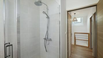 Una ducha moderna con cabezal de ducha manual, panel de control en la pared y puerta de cristal.