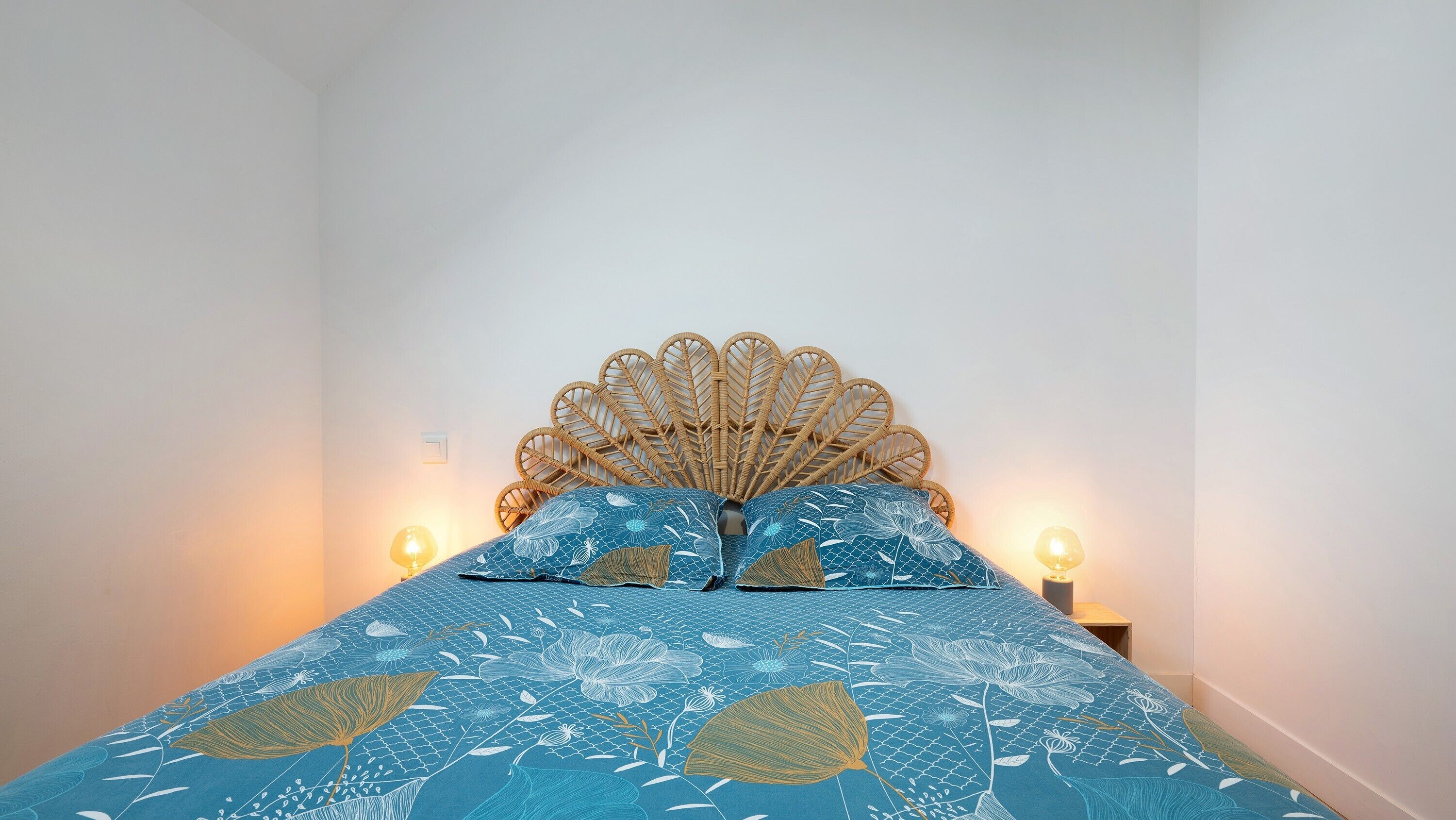 Un lit avec une tête de lit en osier, deux oreillers et des lampes de chevet.