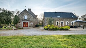 A stone building with a red door, a gravel driveway, and a grassy area in front. - Gîte - Le Buis de Bréhaut: terrace, garden, and Wi-Fi (Taupont)