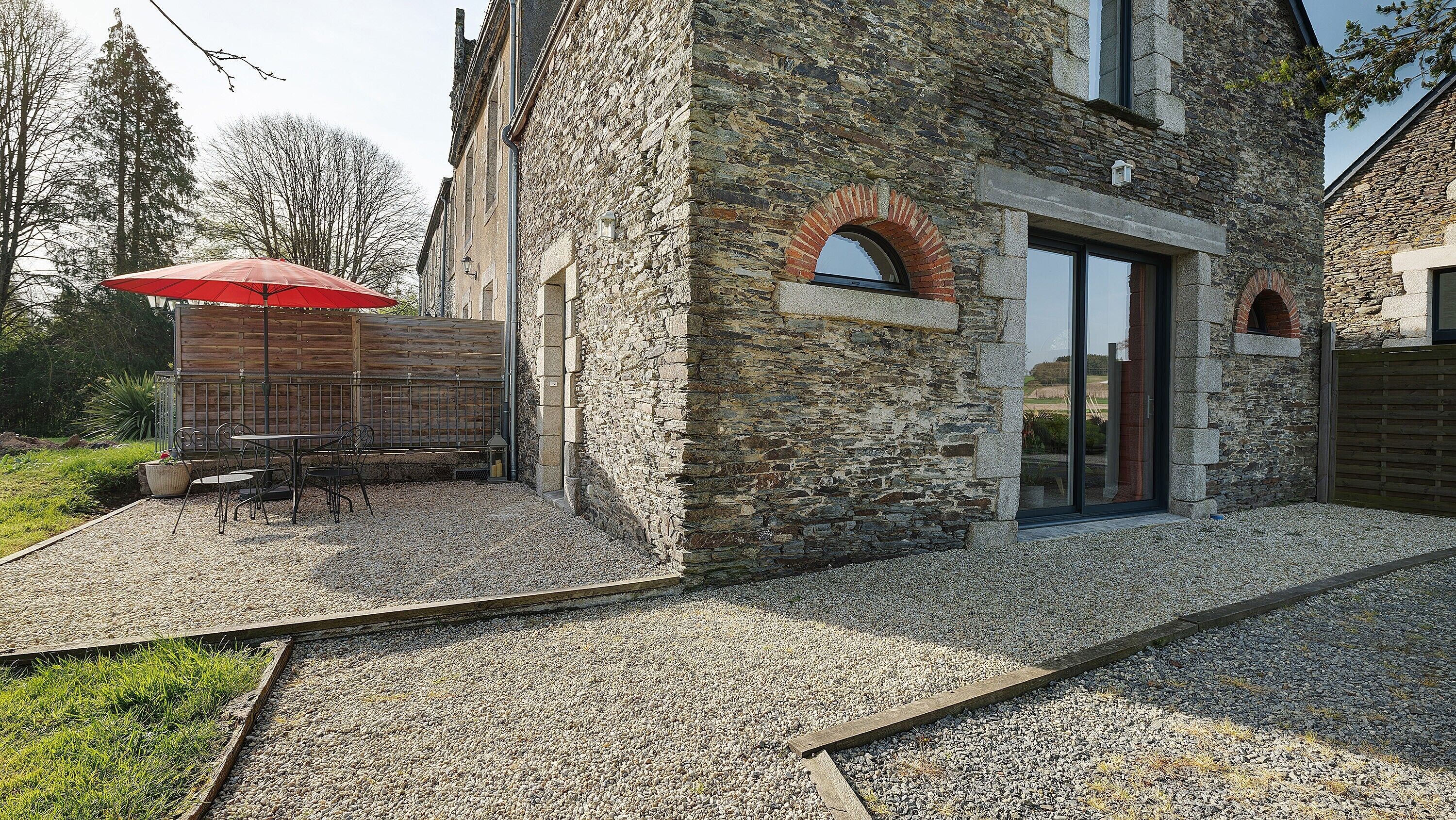 A stone building with a patio, outdoor seating, and a red umbrella.