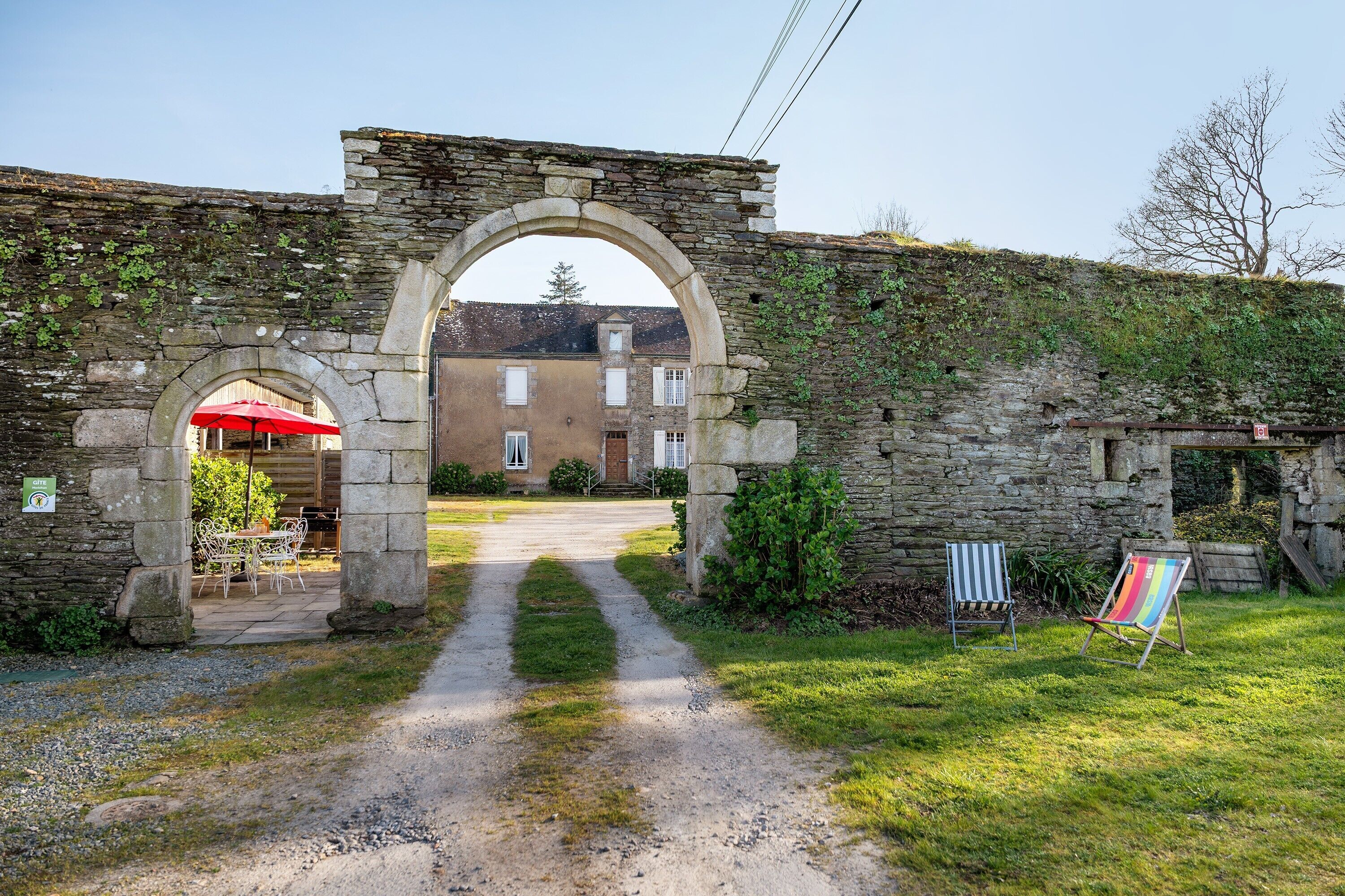 An old stone archway leading to a building with a red umbrella outside.