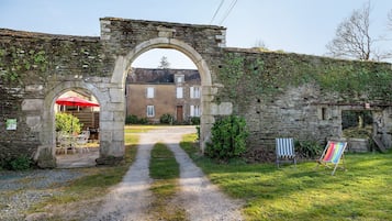 An old stone archway leading to a building with a red umbrella outside.