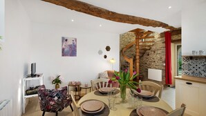 Un comedor con una mesa redonda dispuesta para cuatro, un cuadro en la pared y una escalera que sube a un nivel superior.