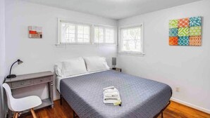 Une chambre à coucher avec un lit, un bureau et une chaise. Il y a deux fenêtres et un luminaire au plafond.