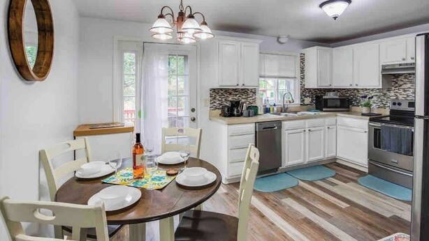 Une cuisine moderne avec des meubles blancs, des appareils en acier inoxydable et une table à manger en bois, accompagnée de chaises.