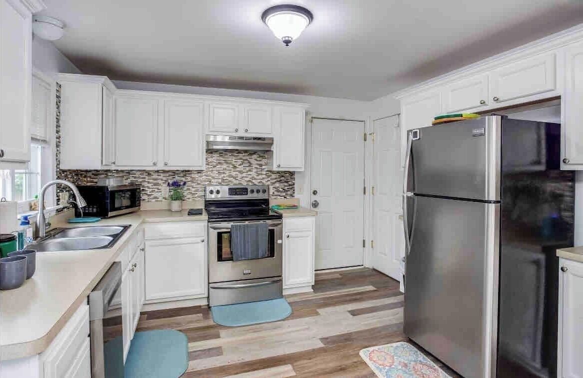 A modern kitchen with white cabinets, a stainless steel refrigerator, a microwave, and an oven.