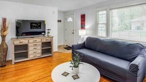 Un salon moderne avec un canapé gris, un meuble en bois doté de tiroirs, un téléviseur à écran plat et une table basse ronde sur laquelle est posée une plante.