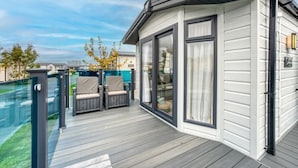 Una terrazza esterna coperta con due sedie e un tavolo, una stanza vetrata con porta scorrevole e una vista libera sui dintorni.