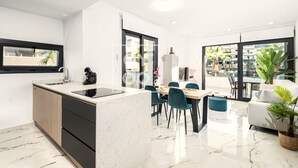 Et moderne køkken med en central ø, et spiseområde med stole, samt en opholdsstue med sofa og plante.